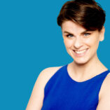 Die Inhaberin des LAX VOX® Institutes Stephanie Kruse vor blauem Hintergrund. Sie zeigt dir in ihren LAX VOX Workshops, wie du mit der Übung LAX VOX deine Stimme trainieren kannst